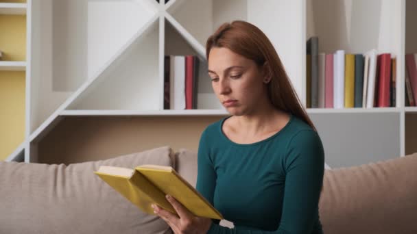 Fiatal nő ül a kanapén otthon. könyv olvasása. — Stock videók