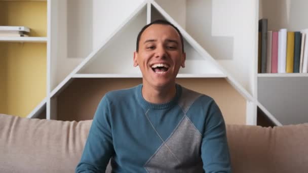 Happy man laughing out loud at humorous joke looking at camera at home, cheerful casual young man with funny face sit on sofa enjoy sincere positive emotions screaming with laughter concept. — Stock Video