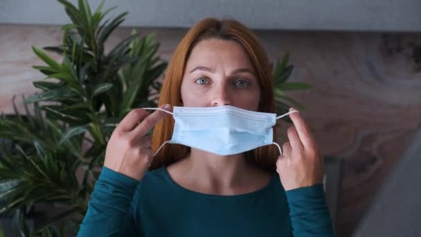 Ung kvinna tar medicinsk mask hemma. Sjukvård och medicinskt koncept. Närbild porträtt . — Stockvideo
