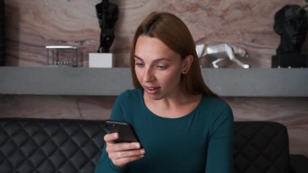 Удивлённая женщина смотрит на смартфон. Закрывая рот, женщина смотрит онлайн-новости на смартфоне. Портрет счастливой девушки торговый сайт на смартфоне — стоковое видео