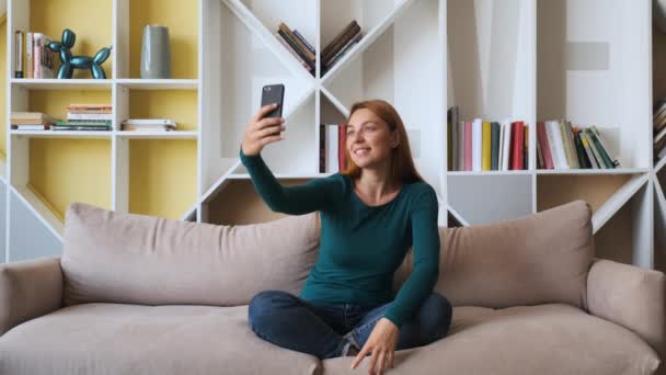 Ung attraktiv kvinna tar bild med sin smartphone sitter på soffan hemma. — Stockvideo