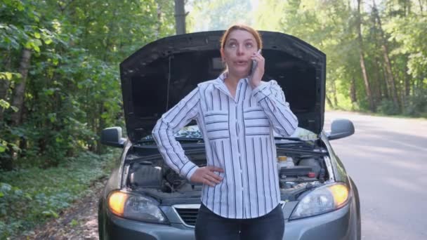 Obchodní žena v pozadí rozbitého auta v lese. Stres ženský řidič stojí před otevřenou kapotou a volat evakuaci. Rozbití, problém. — Stock video
