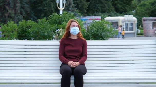Jonge vrouw zit alleen op een parkbank tijdens een epidemie. Veiligheid, afstand, gezondheid, N1H1, virusbescherming, covid, virus en coronavirus — Stockvideo