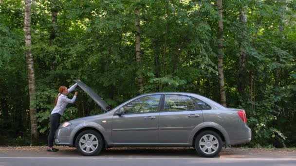 Een jonge vrouw een kapotte auto en opent de motorkap in het bos. De auto stortte plotseling in op een landweg tijdens het rijden. — Stockvideo