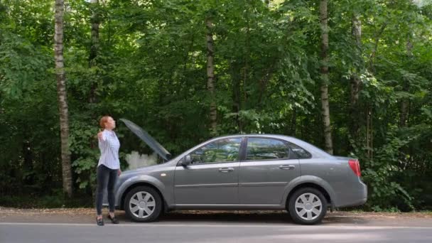 Femme essayant d'arrêter une voiture dans la forêt. Conductrice stressée debout devant le capot ouvert. Cassure, problème — Video