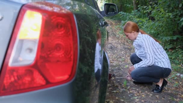 Una mujer tratando de levantar un auto en el bosque. Dama de negocios segura arreglando la rotura del coche sola en la carretera suburbana. Problemas de viaje. — Vídeos de Stock