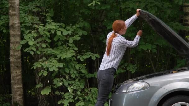 Femme ouvrant capot de voiture et regardant le moteur. Une conductrice debout à côté d'un véhicule cassé près de la forêt. Concept accident de la route. — Video