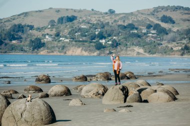 Güzel Asyalı kadın Moeraki Kayaları üzerinde duruyor, Güney Adası, Yeni Zelanda.