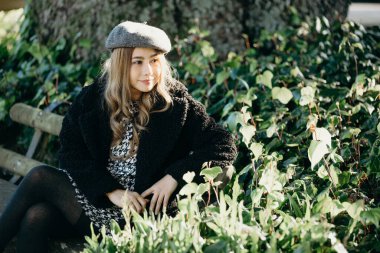 Kadın parkta bir bankta oturuyor, sonbahar parkında boş vakit geçiriyor. Siyah ceketli moda kadını bankta oturuyor..