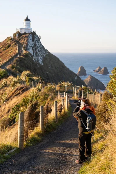 Beautiful asian tourist take some picture at Nugget Point, Dunedin, New Zealand. Young asian traveller enjoys walking in morning along coastline of New Zealand. Lifestyle image with natural landscape.