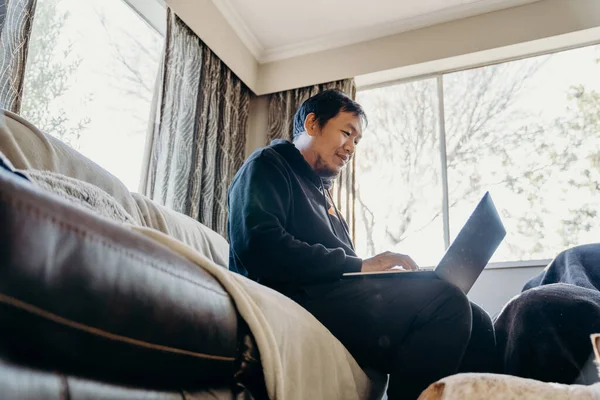 Asian man work from home by laptop with his dog in living room.