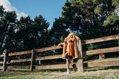 Doğada ahşap bir çitin yanında oturan Asyalı genç bir kadın..