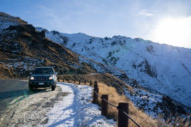 Yeni Zelanda 'daki tepede karlı dağ yolunda bir araba..