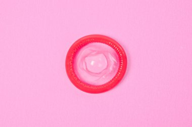 Pembe bir arka plan üzerinde açılan prezervatif.
