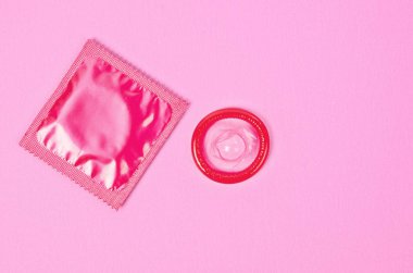 Pembe pembe bir arka plan üzerinde paketindeki prezervatif ve prezervatif açıldı.