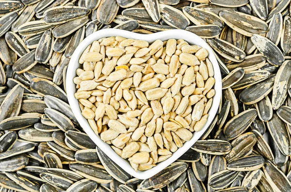 Sunflower seeds in white bowl on sunflower seeds background.