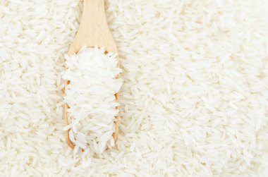 Pirinç arka planında tahta kepçe içinde çiğ beyaz pirinç..