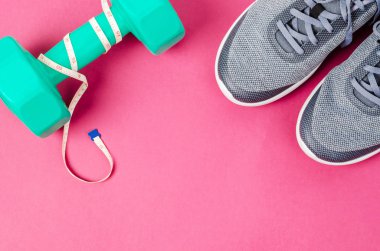 Pembe arka planda yeşil halterler ve spor ayakkabılar. Mesajınız veya mesajınız için boş bir alan. Egzersiz konsepti.