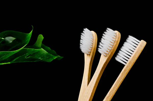 Бамбуковые зубные щетки с зелеными листьями на черном фоне . — стоковое фото