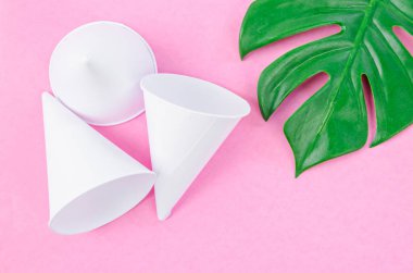 Pembe arka planda yeşil yapraklı tek kullanımlık kağıt külah su bardakları.