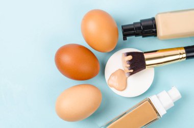 Makyaj süngerleri ve mavi arka planda yumurta üzerine sıvı cam temel şişesi. Cilt konsepti için ton rengi temel makyajı seçin.