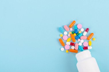 İlaç hapları ve haplar mavi arka planda bir ilaç şişesinden dökülüyor..