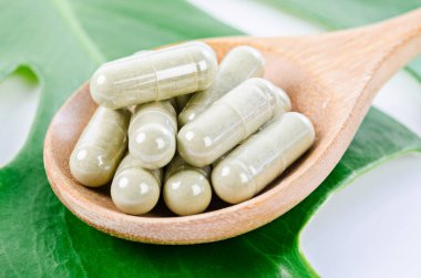 Sağlıklı olmak için yeşil yapraklı ahşap kaşıktaki bitkisel kapsüller. Yaşam tarzı kavramı.