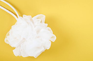 Beyaz duşlu sünger örgüsü, sarı arka planda banyo vücut fırçası..