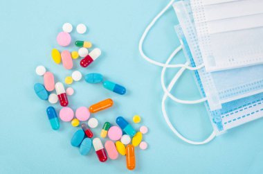 Mavi arka planda cerrahi yüz maskesi olan ilaç ve haplar..