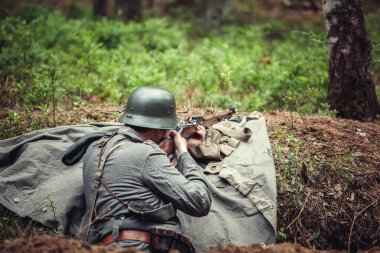 2. Dünya Savaşı, sert şapkalı bir asker ağaçlarda bir tüfek ateşledi. Askeri tarihi yeniden yapılandırma..