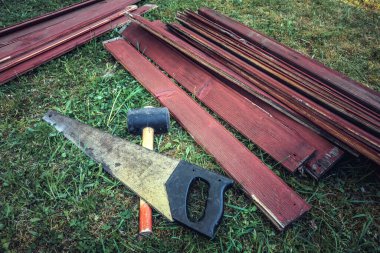 Demir testeresi, kauçuk çekiç ve bahçedeki çimlerin üzerinde tahta tahtalar.