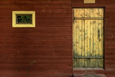 Sarı ahşap bir kapı ve duvarda küçük bir pencere.