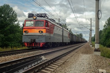 Elektrikli yük treni demiryoluna çıkar ve yük taşıyan vagonları taşır.