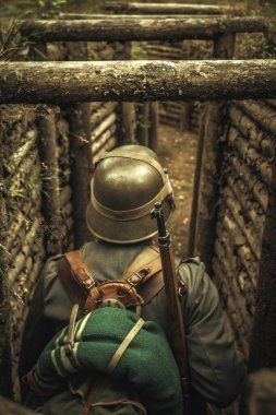 A world war II soldier stands in a wooden trench with a rifle, photo from behind. clipart