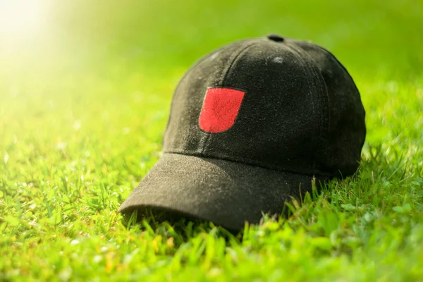 Black baseball cap with a red logo on a summer background