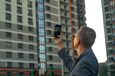 Bir adam telefonuyla çok katlı bir binanın fotoğraflarını çekiyor. Emlak satın almak