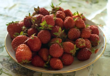 Masanın üzerinde bir tabak kırmızı çilek.