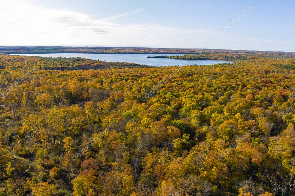Autumn color from trees with a lake in the background in Door County Wisconsin from a drone