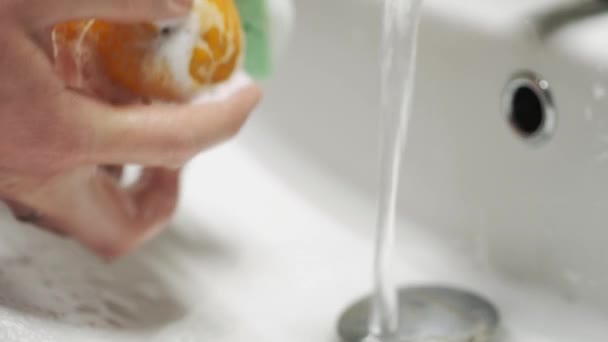 Close-up van de handen was de sinaasappel onder stromend water. Oranje zeepspons wassen. — Stockvideo