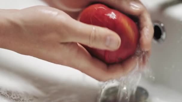 Kırmızı bir elmayı akan suyun altında yıkayan ellere yakın çekim. Sağlıklı ve temiz yiyecekler. — Stok video