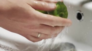 Yakın plan çekimde akan suyun altında yeşil biberi yıkayın..