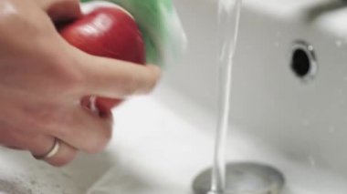Kırmızı bir elmayı akan suyun altında yıkayan ellere yakın çekim. Sağlıklı ve temiz yiyecekler.