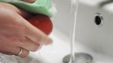 Beyaz lavaboda akan suyun altında domates yıkayan eller..