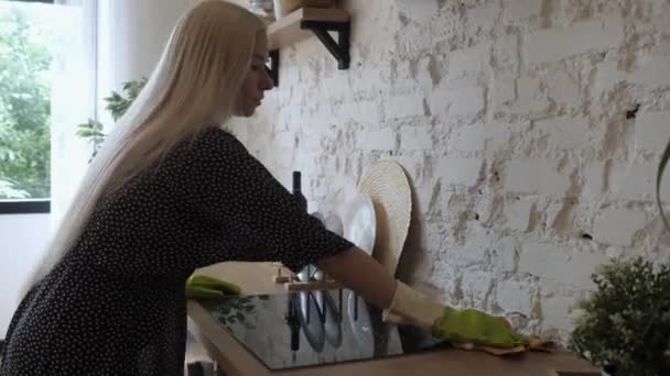 Jeune femme au foyer porter des gants de protection en caoutchouc nettoie le panneau de cuisson. 4K — Video