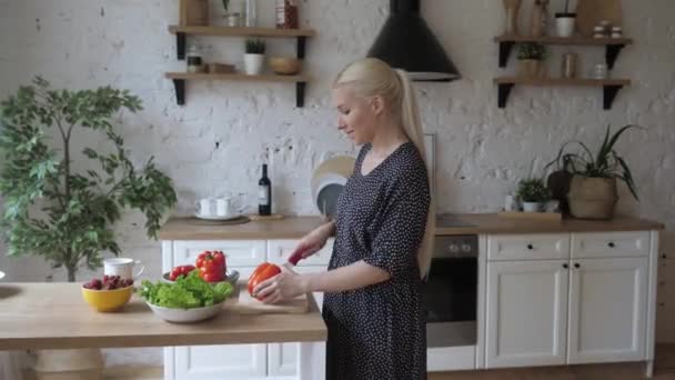 Belle jeune femme au foyer tient des coupes de couteau poivre salade cuisine plat de légumes. — Video