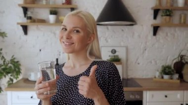 Mutfakta elinde bir bardak suyla duran bir kadın baş parmağıyla gülümsedi.