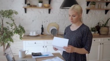 Mutfakta duran genç bir kadın elektrik faturasını açıyor ve çok üzgün.