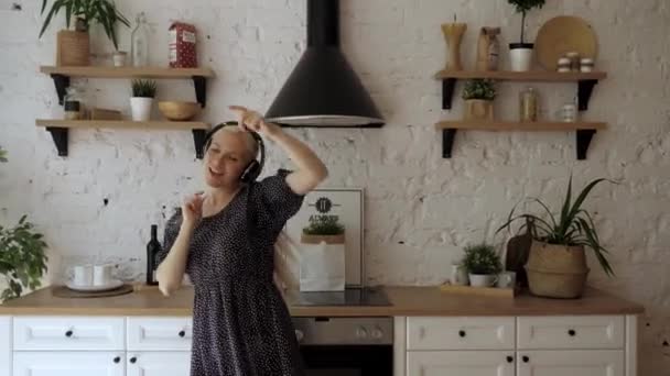 Hermosa mujer escuchando música en los auriculares y bailando divertido en la cocina — Vídeos de Stock