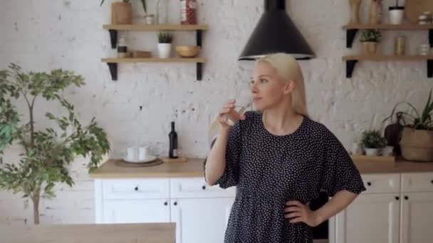 Het meisje drinkt water uit een glas dat in de lichte keuken staat. — Stockvideo