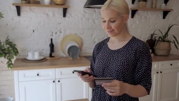 Femme debout dans une cuisine blanche entre les données d'une carte en plastique dans le téléphone — Video